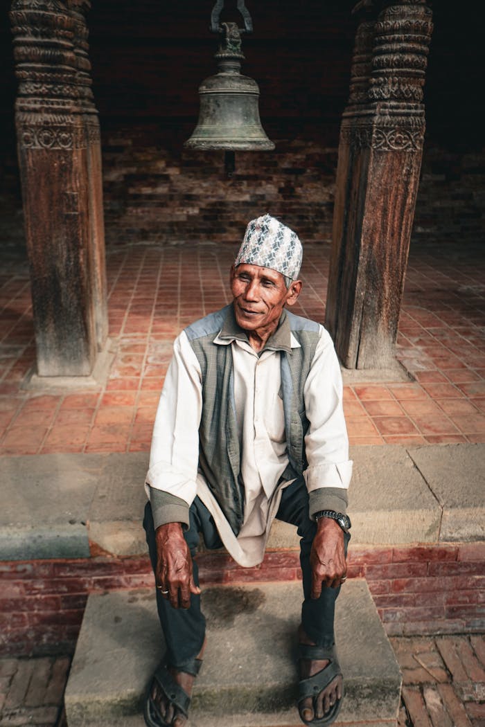 An elderly man in traditional attire sits on temple steps in Nepal.